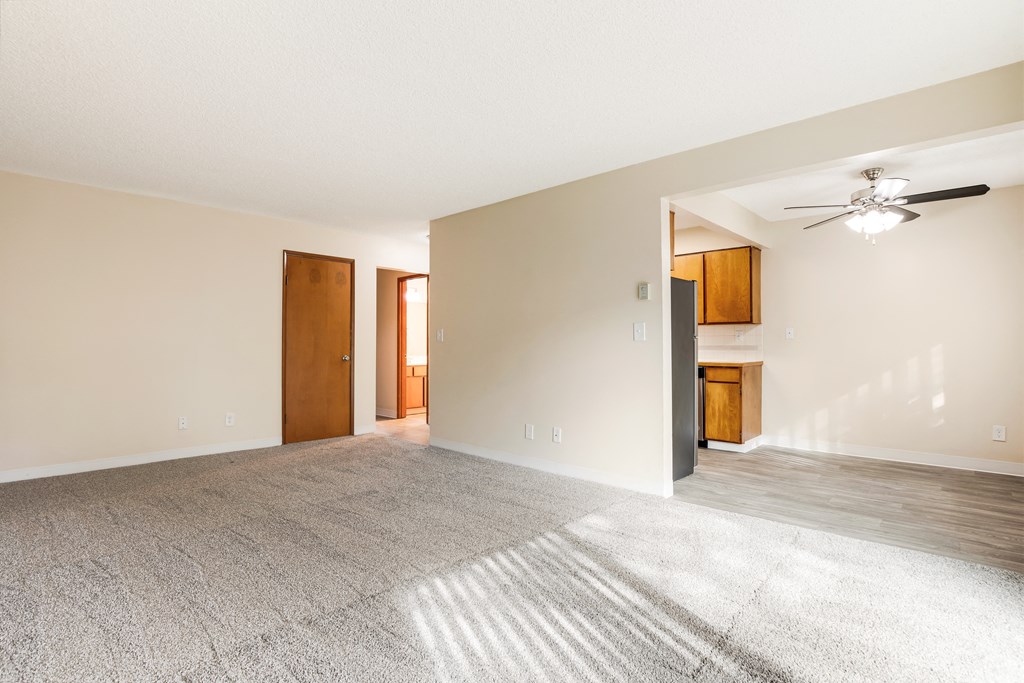 an empty living room with a ceiling fan and a door to a kitchen