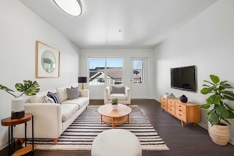 A living room with a white couch, a wooden coffee table, and a flat-screen TV mounted on the wall.