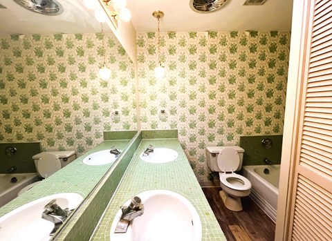 A bathroom with green tiles and a green and white patterned wallpaper.