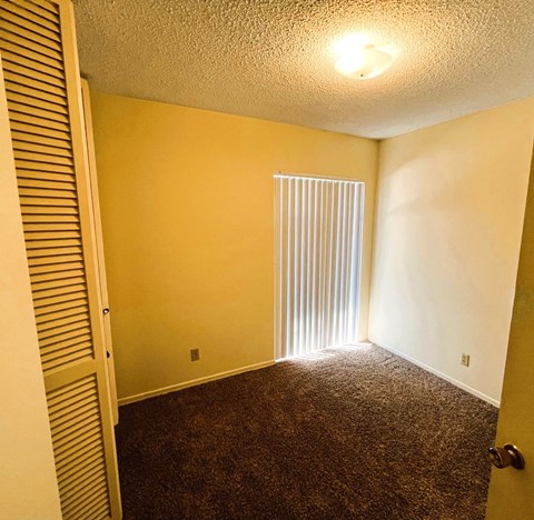 A room with a carpeted floor and a window with blinds.