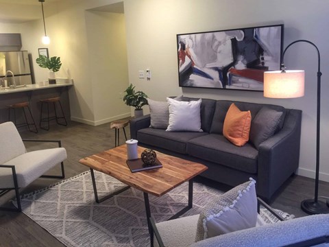 A modern living room with a grey couch, a wooden coffee table, and a large painting on the wall.