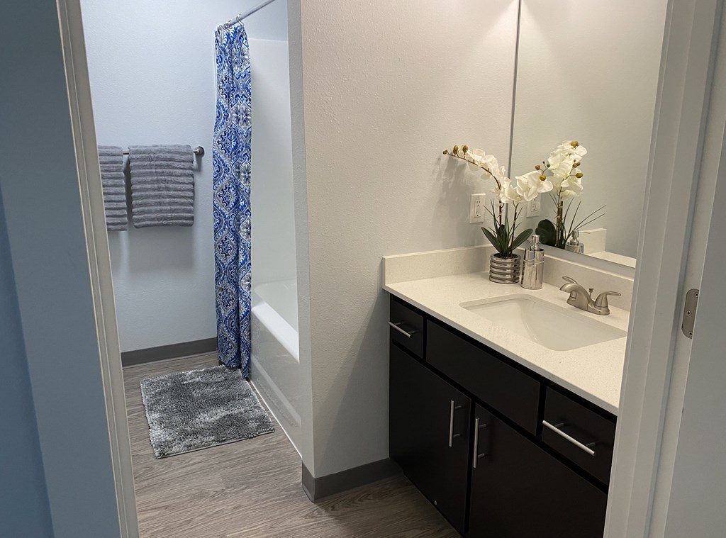 A bathroom with a sink, mirror, and a shower with a blue curtain.