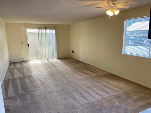 A spacious room with a carpeted floor and a ceiling fan.