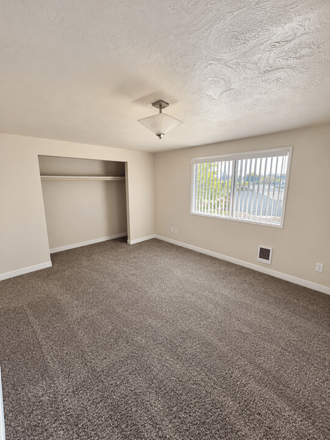 A room with a carpeted floor and a window with blinds.