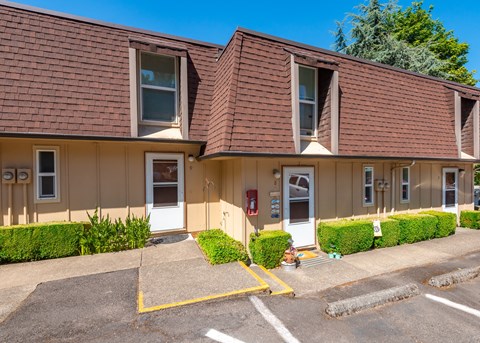 the front of a tan building with two windows and a parking lot
