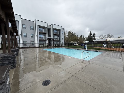 A wet swimming pool area in front of apartment buildings.