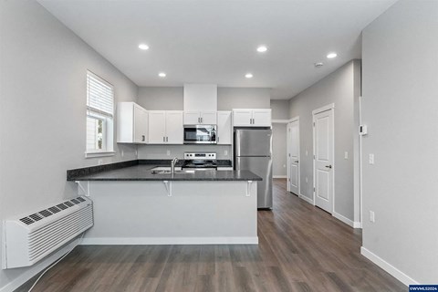 A modern kitchen with white cabinets and a wooden floor.