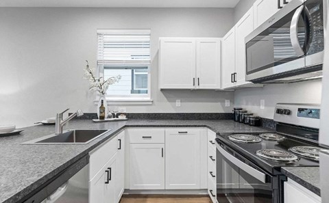 A kitchen with white cabinets and black countertops.