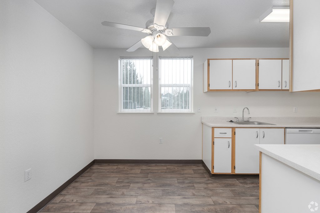 A room with a fan and a kitchen area with cabinets and a sink.