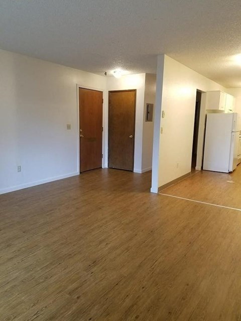 an empty living room with a refrigerator and a door