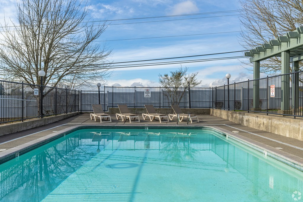 A pool surrounded by a fence with sun loungers on the side.