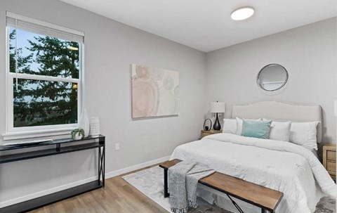 A bedroom with a large bed and a window overlooking a tree.
