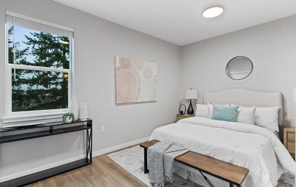 A bedroom with a large bed, a window with a view of trees, and a painting on the wall.