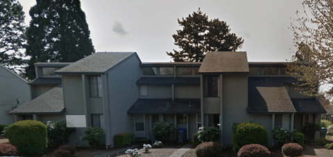 A grey building with a black roof and a tree in front.