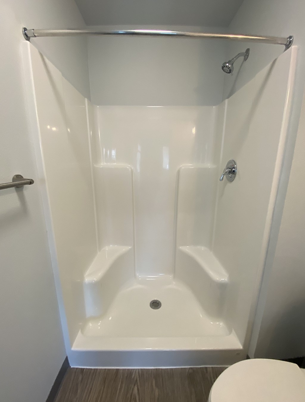 A white shower stall with a towel bar and a drain.