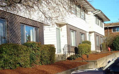 A house with a white front and a brown hedge.