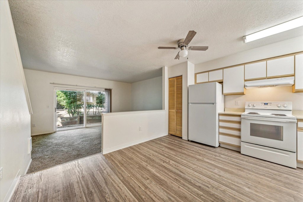 an empty kitchen with white appliances and a ceiling fan