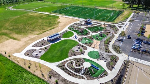A park with a green lawn, a basketball court, a tennis court, a soccer field, and a playground.