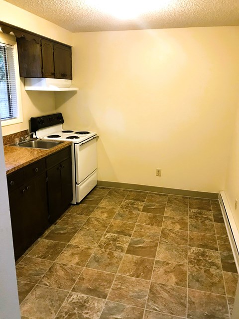 A kitchen with a white stove and brown tiled floor.