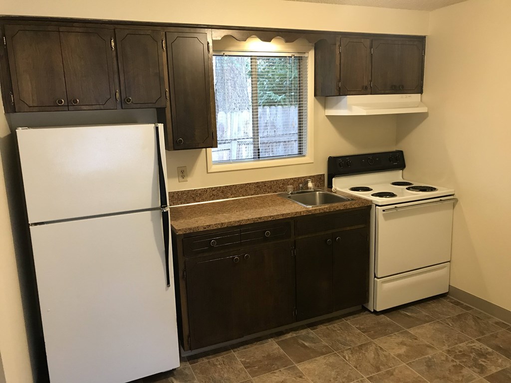 A kitchen with a white refrigerator, brown cabinets, and a white stove.