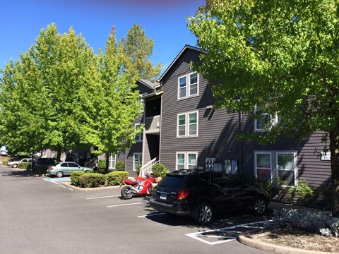 A black car is parked in a parking lot in front of a grey building.