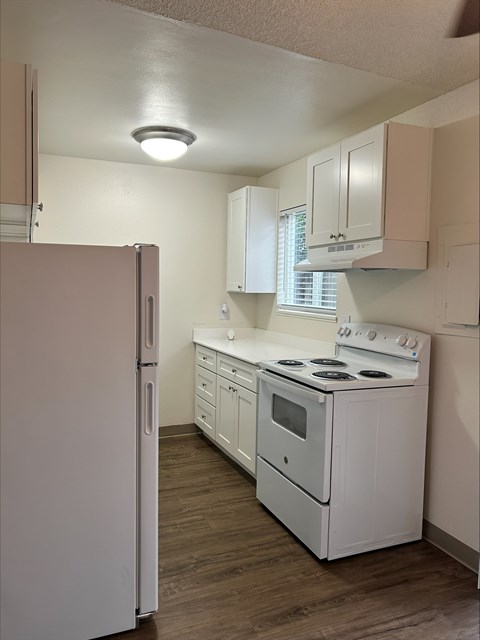 A white refrigerator is in a kitchen with wooden floors.