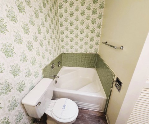 A white toilet sits next to a bathtub in a bathroom with green wallpaper.