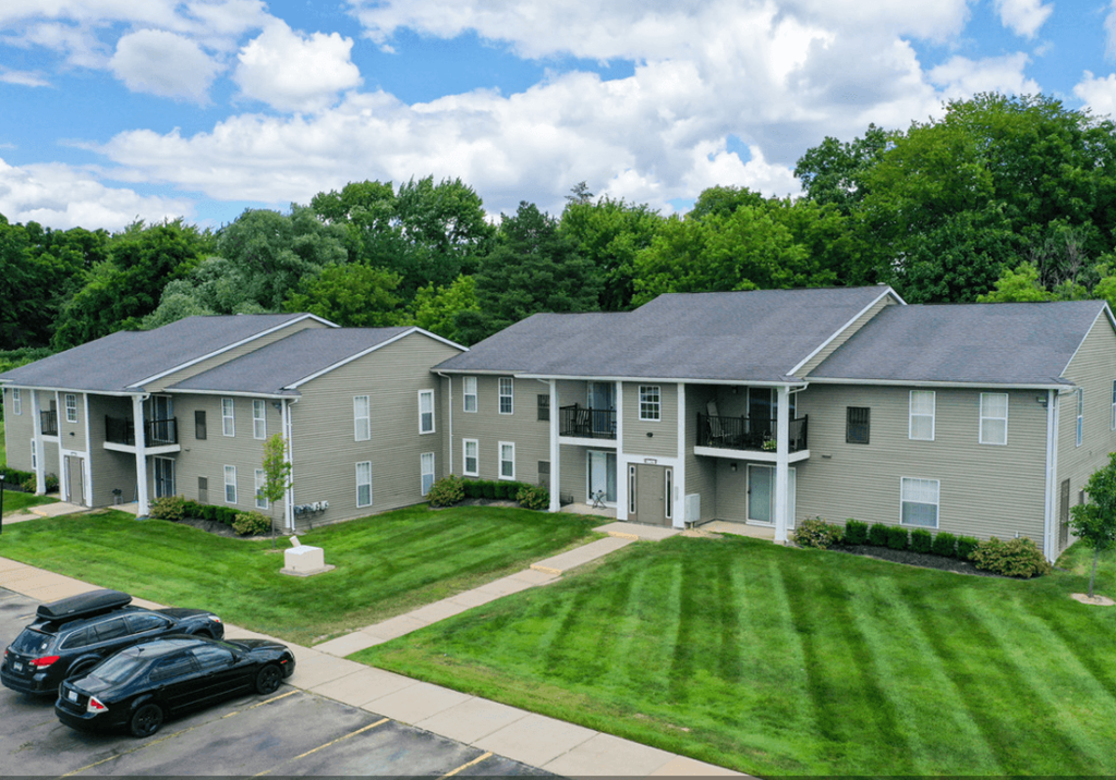 an aerial view of an apartment complex with cars parked in front of the lawn