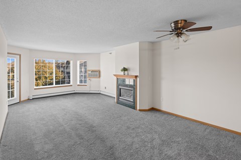 A living room with a grey carpet and a ceiling fan.