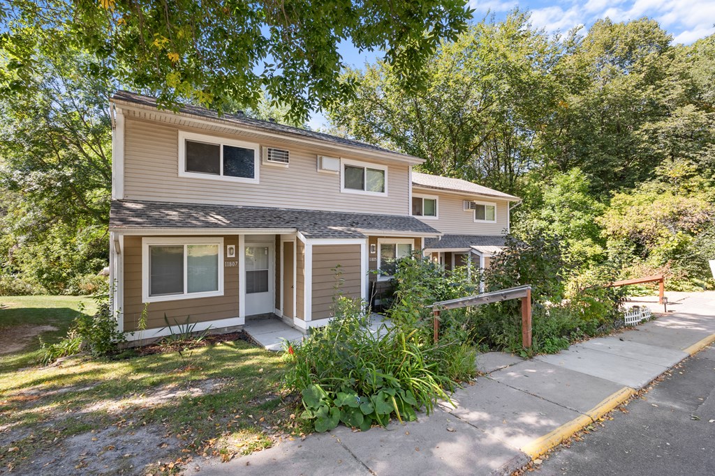A two-story house with a brown and beige exterior is surrounded by greenery.