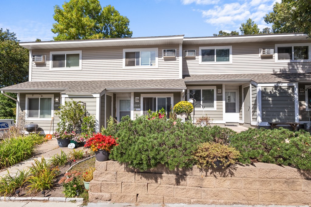 A house with a grey siding and a brown roof with a garden in front.