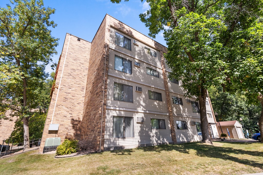 A tall building with a mix of brick and siding exterior is surrounded by trees.