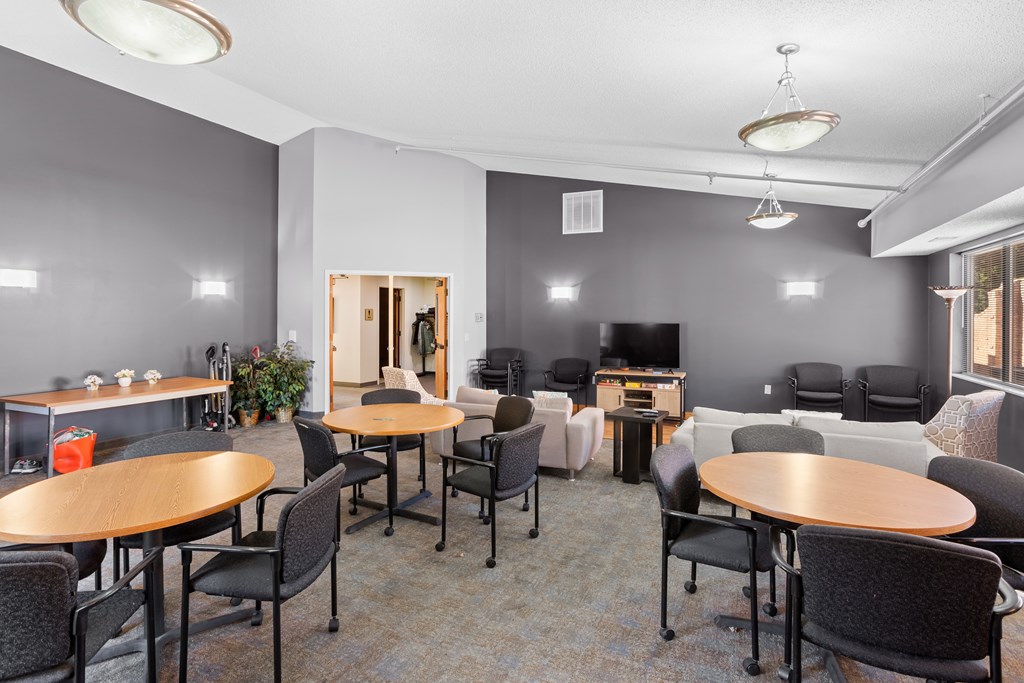 A room with grey walls and a carpeted floor has a table and chairs in it.
