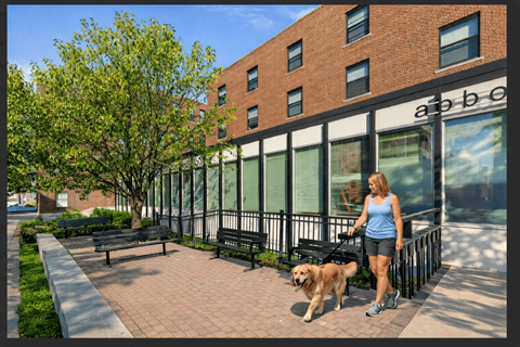 A woman walking her dog in front of a brick building.