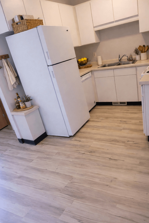 A white refrigerator stands in a kitchen with wooden flooring.