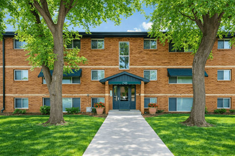 A brick building with a green awning and a tree in front.