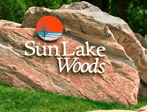 A large rock with the words Sun Lake Woods written on it.