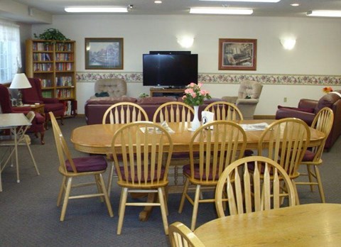 A room with a wooden table surrounded by chairs and a television on the wall.