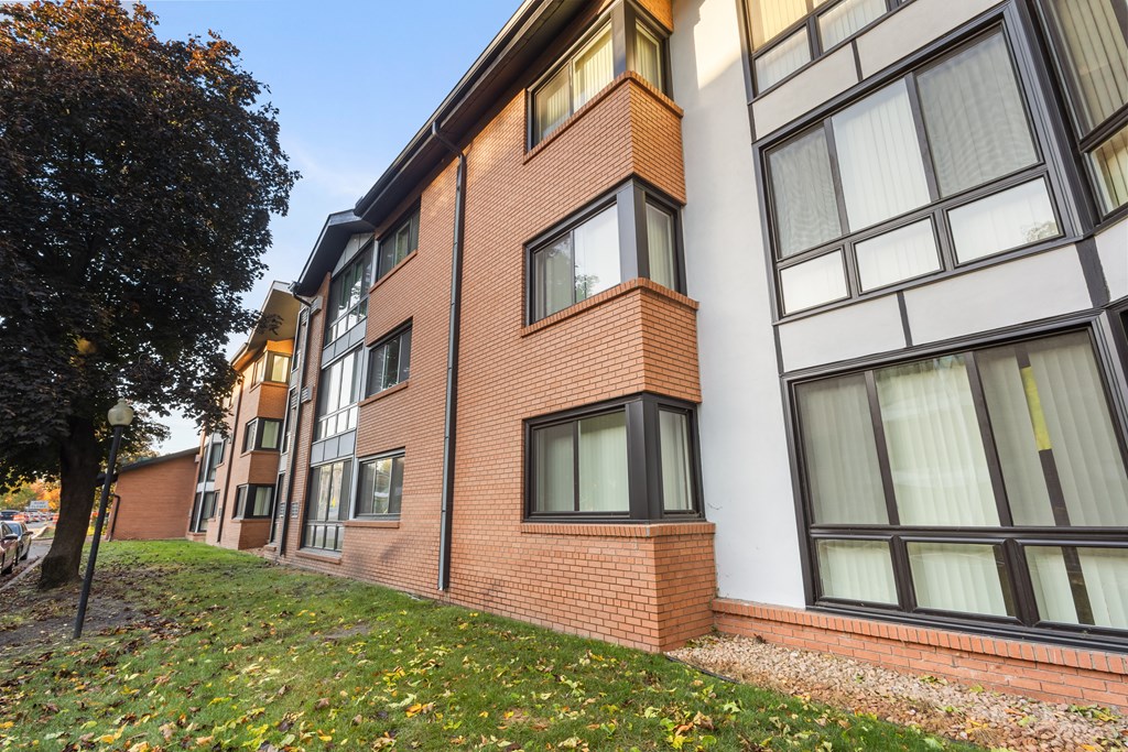 A red brick building with white windows and a tree in front.
