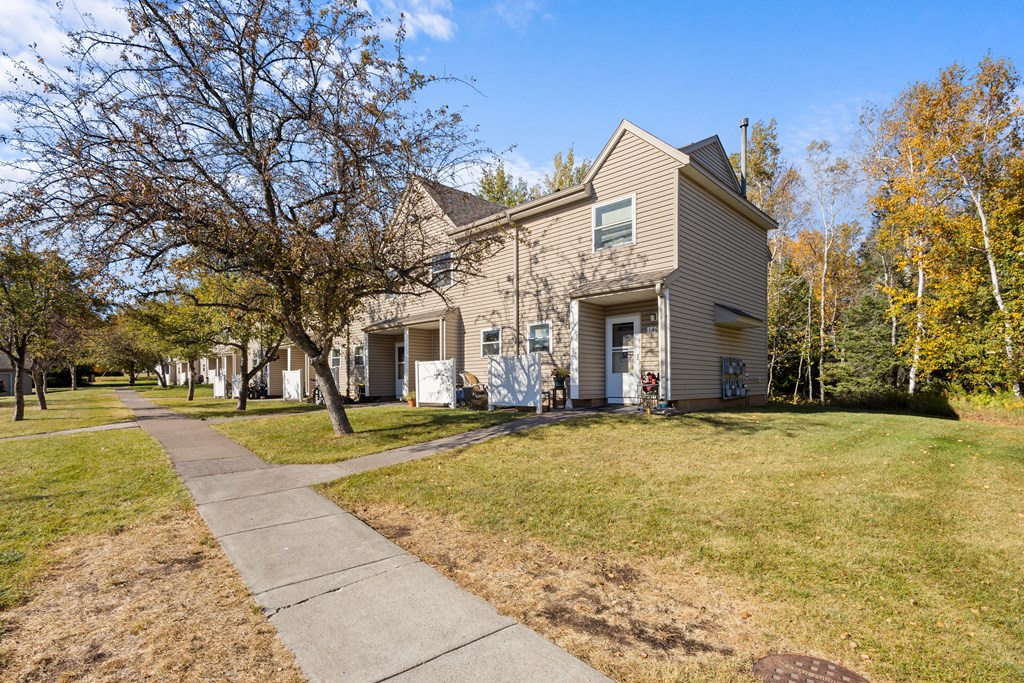A house with a grey roof and white trim is surrounded by trees with yellow leaves.