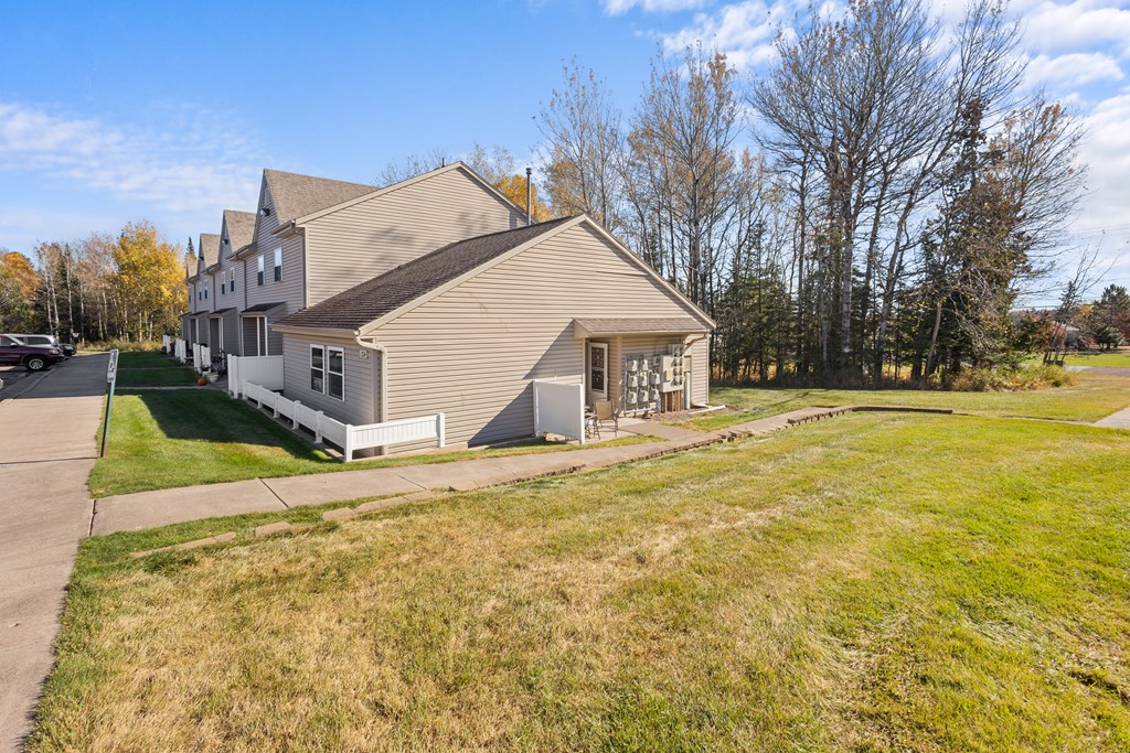 A house with a grey roof and white fence is surrounded by a grassy area.