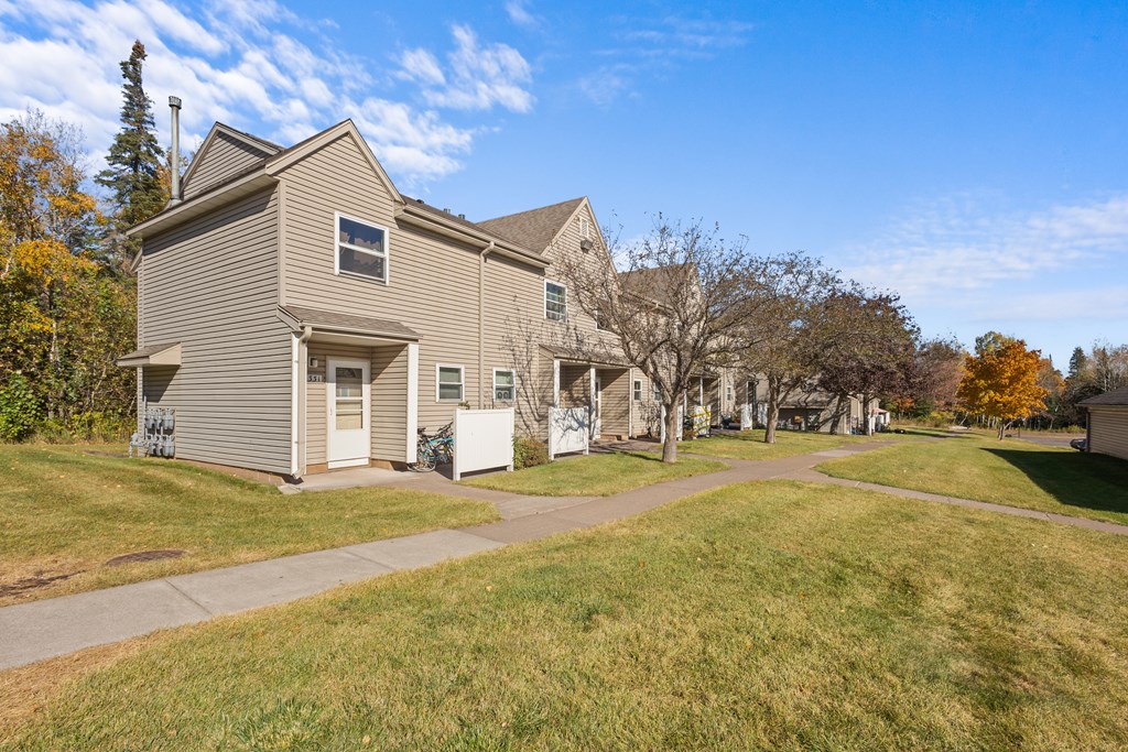 A house with a brown roof and a white door is surrounded by trees with yellow leaves.