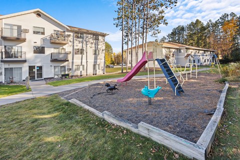 A playground with a slide and swings in a grassy area.
