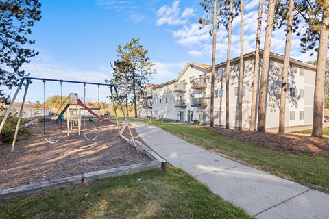 A playground with a swing set and a building in the background.