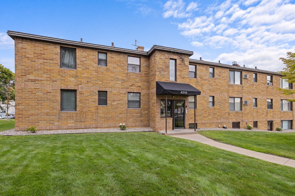 A brick building with a black awning and a sign that reads "411" is surrounded by a grassy lawn.