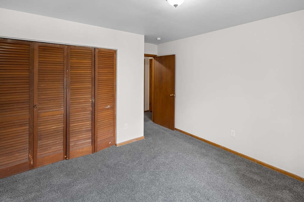 A room with a carpeted floor, a white wall, and a brown door.