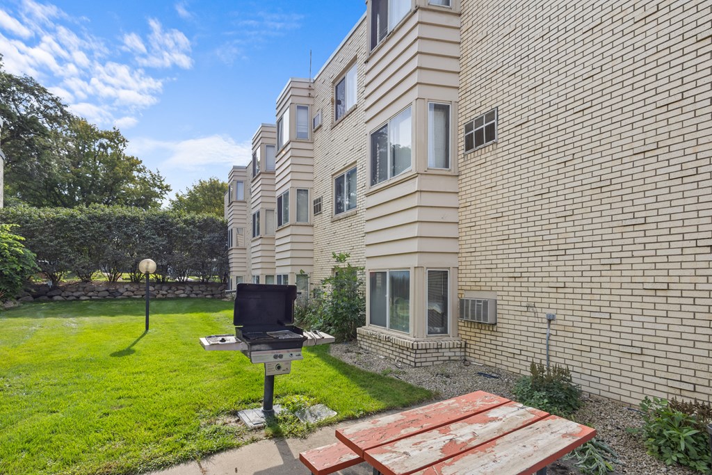 A BBQ grill is on a patio in front of a brick building.