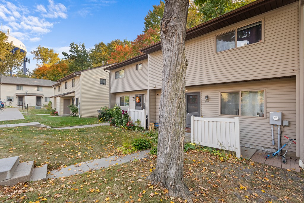 A tree stands in front of a building with a white fence.