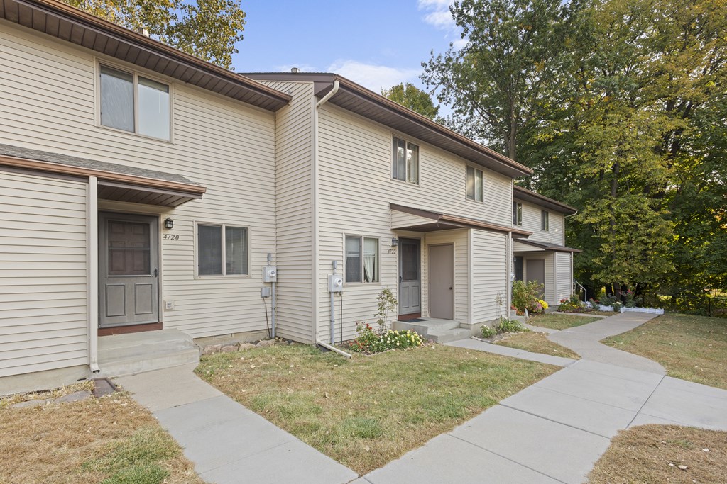 A beige two-story apartment building with a brown roof and a small front yard.