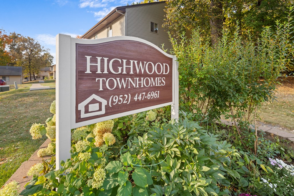 A sign for Highwood Townhomes stands in front of a building and some trees.